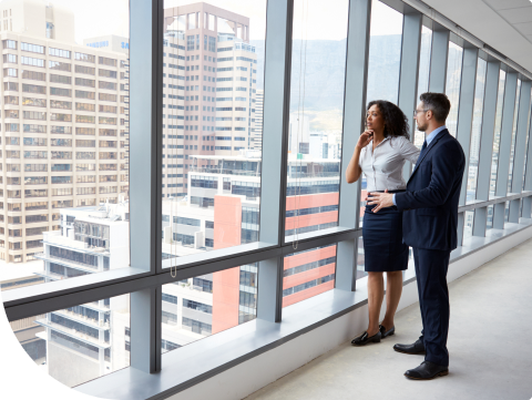 Two businesspeople staring out large window of commercial building