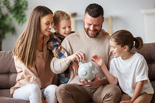 young family of four tucking money away into piggy bank