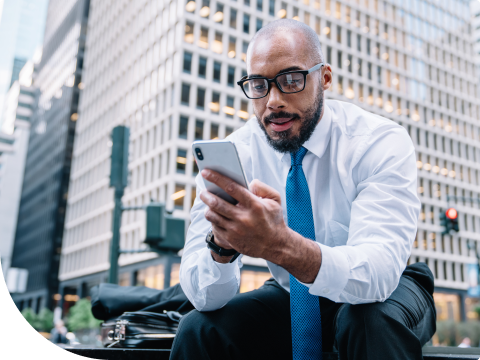 Businessman checking banking transactions while sitting in the middle of the city on his smartphone