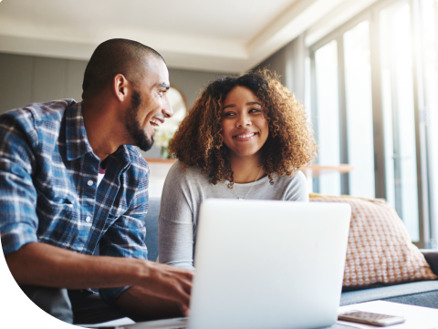 young couple looking happily at their finances on their laptop at home