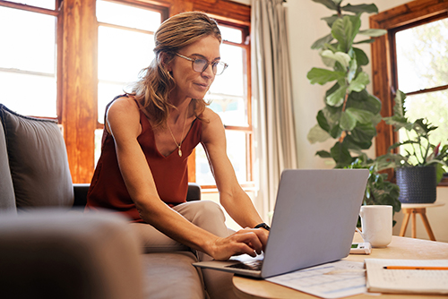 young woman sitting on couch logging into finances on laptop