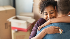man and woman holding keys hugging with moving boxes in the background