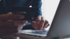 person typing on a laptop holding a credit card