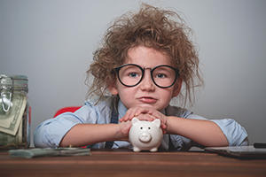 young child wearing glasses leaning head on piggy bank