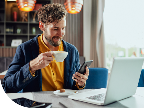 man drinking coffee in front of laptop with cell phone