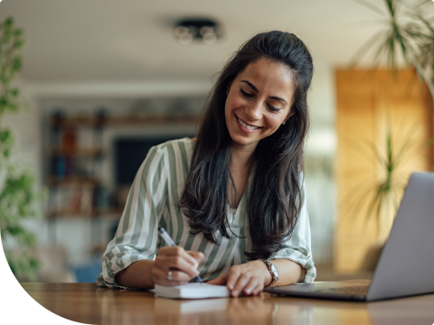 Woman writing out check and looking at laptop